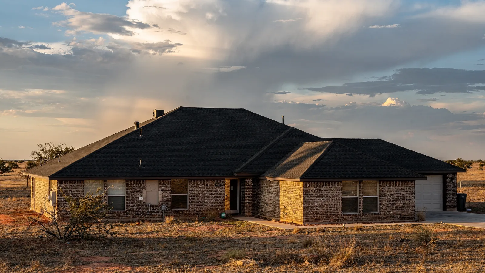 A West Texas brick home with a new charcoal shingle roof under a South Plains storm sky